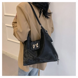 Detail of matte black PU tote with gold bow buckle and chain strap on a khaki blazer