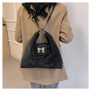 Detail view of black velvet handbag with silver metal bow on beige blazer outfit
