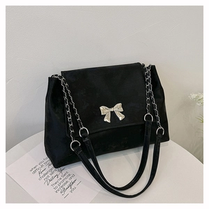 Detail of black velvet shoulder bag featuring a silver bow buckle and metal chain strap