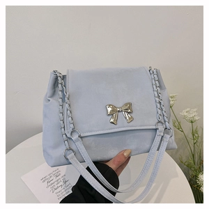 Close-up of a light blue suede handbag with a decorative metal bow clasp and chain strap