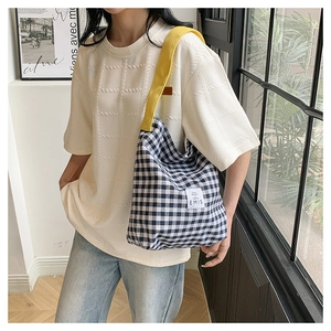 Détail du sac bandoulière en toile à carreaux bleus avec sangle jaune et étiquette