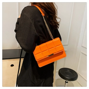 Detail of a bright orange quilted crossbody bag with a gold rectangular metal buckle