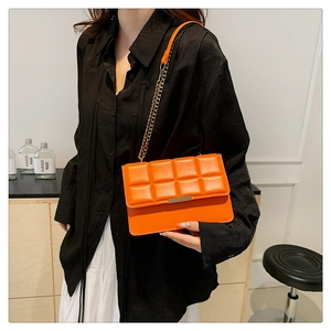 Close-up of bright orange textured crossbody bag with gold chain strap and flap closure
