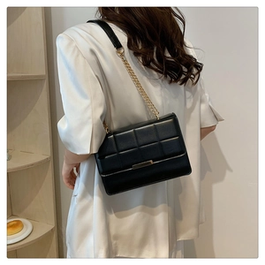 Detail of black quilted crossbody bag with gold chain strap and metal trim on model