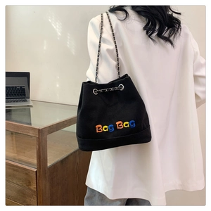 Gros plan sur un sac seau en toile noire avec texte brodé coloré et bandoulière chaîne
