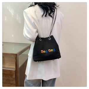Détail du sac seau en toile noire avec broderie de lettres colorées et bandoulière chaîne