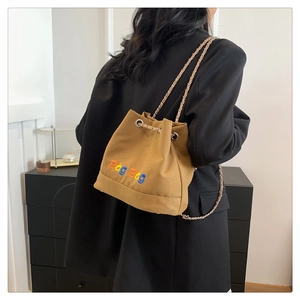 Détail du sac seau en toile marron avec broderie colorée et bandoulière chaîne sur le modèle