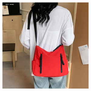 Detail of red nylon crossbody bag with black dual zippers and wide strap on model