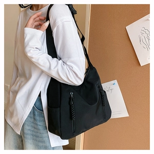 Side view of large black nylon tote bag with unique woven zipper pull on cork background