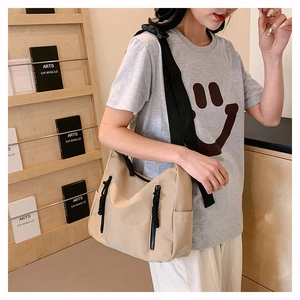 Detail view of a beige nylon tote bag with black zippers shown on a shoulder
