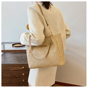 Detail of woven straw tote bag with leather handles and decorative gold chain