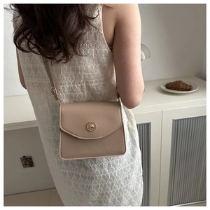 Détail d'un petit sac bandoulière beige en cuir avec boucle ronde en métal doré