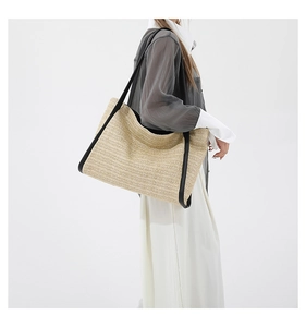 Detail of hand-woven straw tote bag with black contrast trim and long shoulder strap