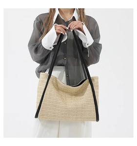 Detail of woven straw tote bag featuring wide black shoulder straps and natural texture