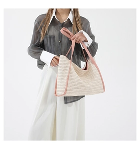 Close-up of woven straw tote bag featuring contrast pink straps and textured fiber detail