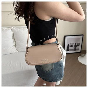 Detail of beige minimalist leather saddle bag with Fashion lettering on model's shoulder
