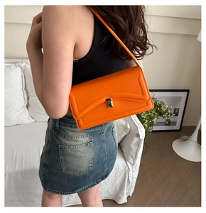 Close-up of vibrant orange shoulder bag with golden metal buckle and smooth faux leather