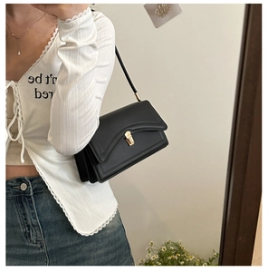 Detail of a black leather crossbody bag featuring gold buckle and accordion-style compartments