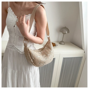 Close-up of floral embroidery on a beige woven crescent bag with wide shoulder strap