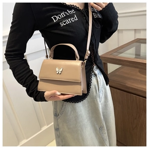 Detail of light brown crossbody bag featuring a golden butterfly buckle and leather texture
