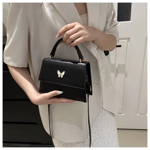 Detail shot of black matte leather handbag with white butterfly hardware and gold buckle