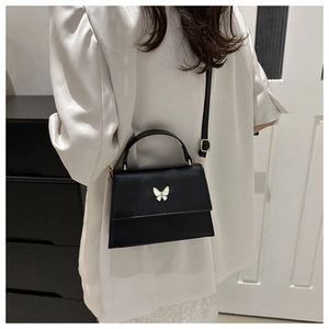 Detailed view of black crossbody bag with white butterfly clasp on white blazer