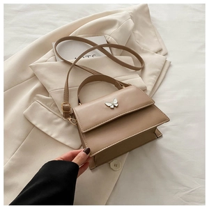 Detail of khaki PU leather bag with white butterfly relief on beige blazer backdrop