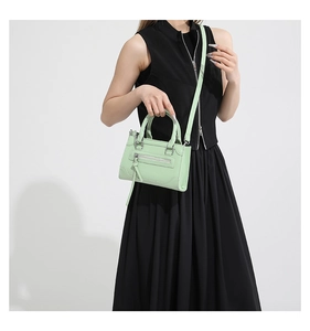 Petit sac bandoulière vert menthe en cuir avec pompons décoratifs porté par un mannequin