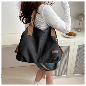 Detailed view of black canvas tote bag with brown straps and fashion patch tag