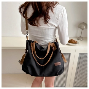 Rear view of a casual black canvas tote bag with brown straps in a minimalist setting