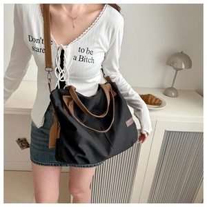 Detail of black canvas tote bag with brown straps and adjustable shoulder strap on model