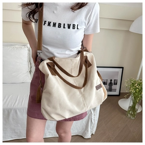 Detail of a beige canvas tote bag with brown straps and a leather logo label on the front