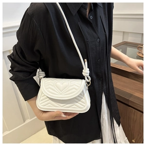 Detail of white quilted handbag featuring heart stitching and knotted strap design