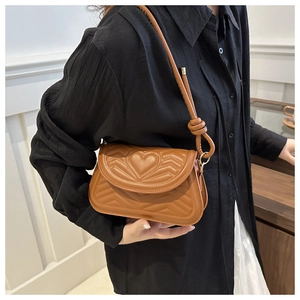 Close-up of caramel saddle bag featuring heart-shaped stitching and knotted strap detail