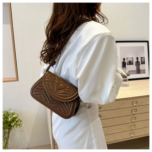 Brown quilted underarm bag with heart chevron embroidery worn by model in home setting