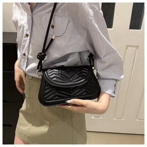 Close-up of black quilted shoulder bag featuring heart and V-pattern embossing with knotted strap