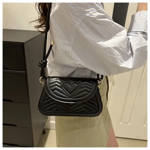 Close-up of quilted black leather shoulder bag with heart pattern and knotted strap