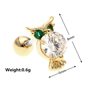 Macro detail of golden owl ear stud featuring green gem eyes and a white cubic zirconia