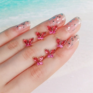 Close-up of six rose red zircon butterfly charms on hand with a soft beach background