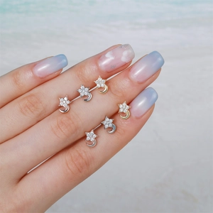 Detailed view of 18k gold and silver star moon stud earrings held by a hand