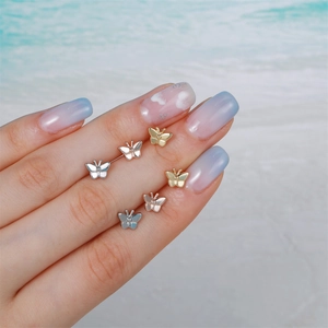Three pairs of small butterfly stud earrings in gold, silver, and rose gold on a model finger