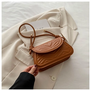Detailed view of the caramel brown heart-quilted leather underarm bag on a beige blazer