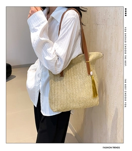 Detail of straw tote bag featuring brown leather strap and vibrant yellow tassel accent