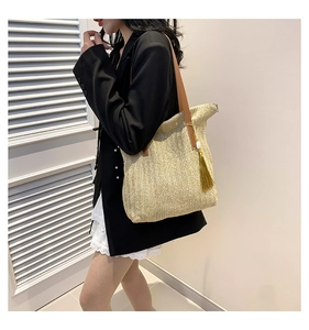 Détail d'un sac en paille avec lanières en cuir marron et pendentif pompon doré