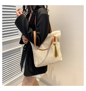Détail du cabas en paille avec bandoulières en cuir marron et pompon jaune élégant