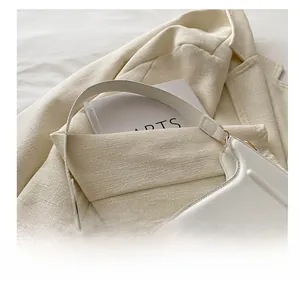 Dettaglio borsa baguette in pelle bianca con logo dorato su giacca di tweed