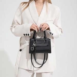 Petit sac à main classique en cuir noir avec poignées et pompons porté par un mannequin