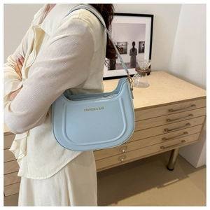 Dettaglio borsa hobo azzurra con logo dorato su cassettiera in legno, scena lifestyle