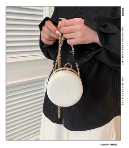 Detail of round ivory evening bag with marble texture and gold chain link strap