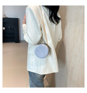Close-up of light blue pleated round bag with gold chain strap worn by a model